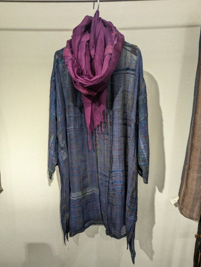絹からみ織りコートと紫色のスカーフが掛けられた展示用の衣服。コートは多色の絹糸で織られ、美しい光沢がある。